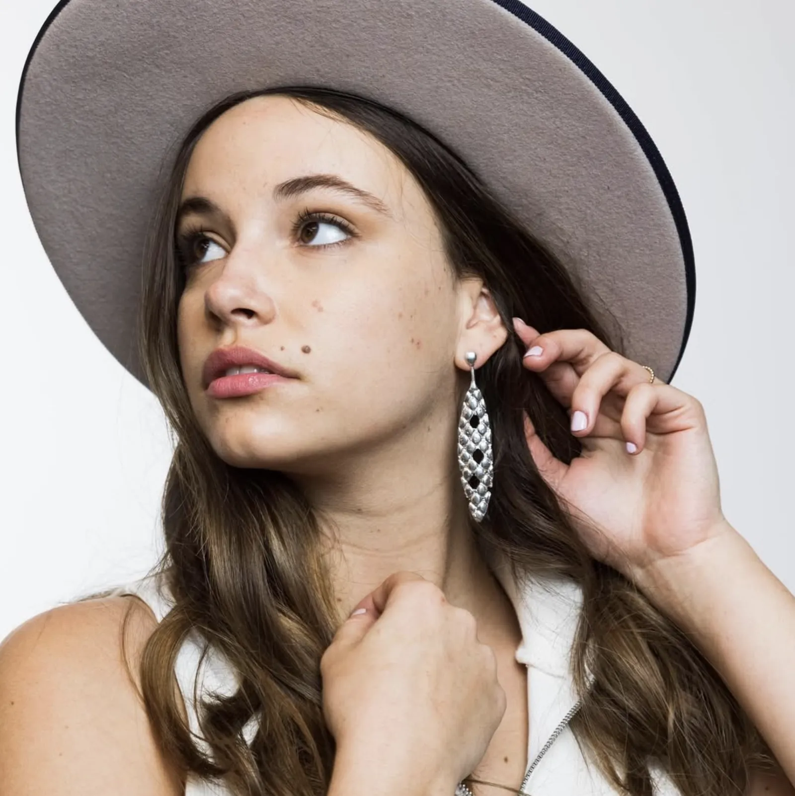 Model in a wide-brimmed hat wearing a long textured silver drop earring