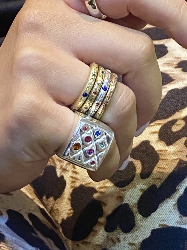 Hand wearing stacked gold rings and a wide silver ring set with colored stones