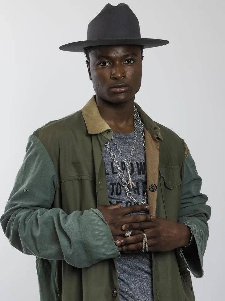 Model in a hat and green coat wearing layered chains and rings