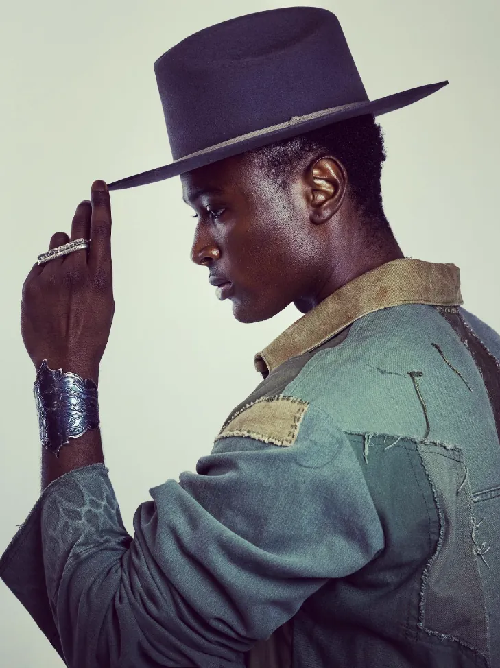 Model in profile tipping a hat, wearing a wide silver cuff and ring